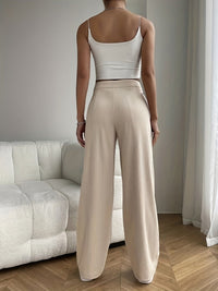 Frau in weißem Top und beigen, plissierten Hosen im Wohnzimmer, moderne Mode, minimalistisch.