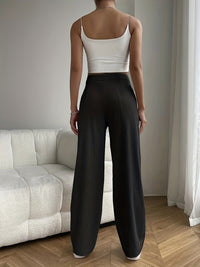 Frau in weißem Crop-Top und schwarzen, gestreiften Hosen im Wohnzimmer.