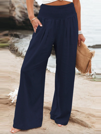 Frau in blauer, weiter Hose am Strand, hält beige Tasche, Sommermode, Damenbekleidung.