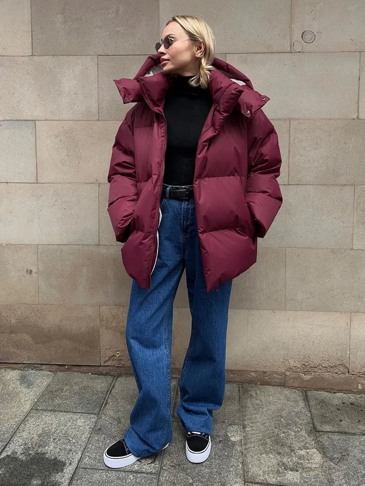 Frau in bordeauxroter Daunenjacke, schwarze Sonnenbrille, blaue Jeans, schwarze Sneaker.