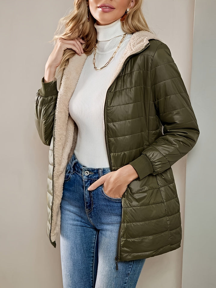Frau in olivgrüner Steppjacke mit Kapuze, weißem Rollkragenpullover und blauer Jeans.