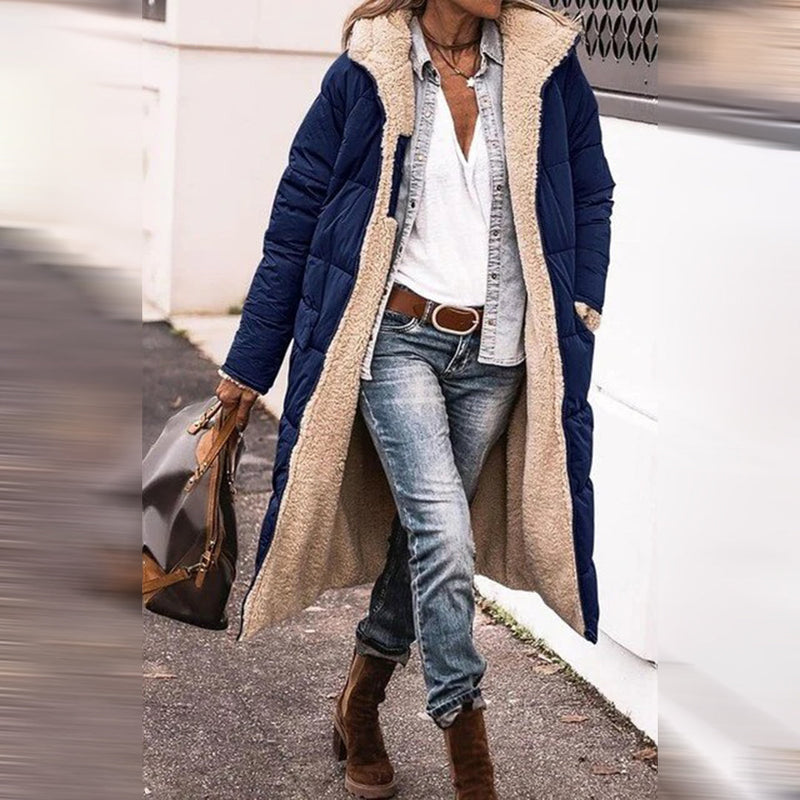 Frau in blauer Winterjacke mit Fellfutter, Jeans und Stiefeln auf Gehweg.