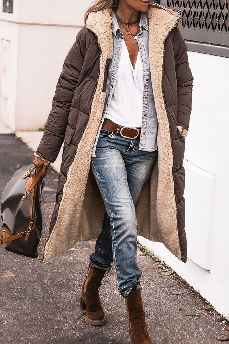 Frau in braunem Daunenmantel mit Lammfellfutter, Jeans und Stiefeln, trägt braune Tasche.