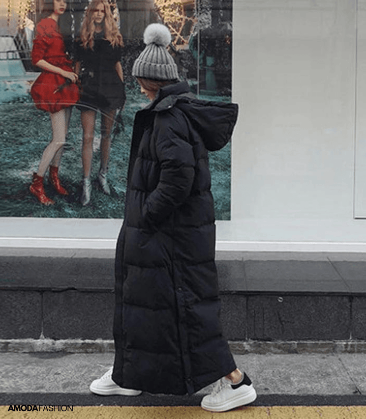 Frau im schwarzen, übergroßen Winterparka mit Kapuze, graue Mütze, weiße Sneaker, Stadtstraße.