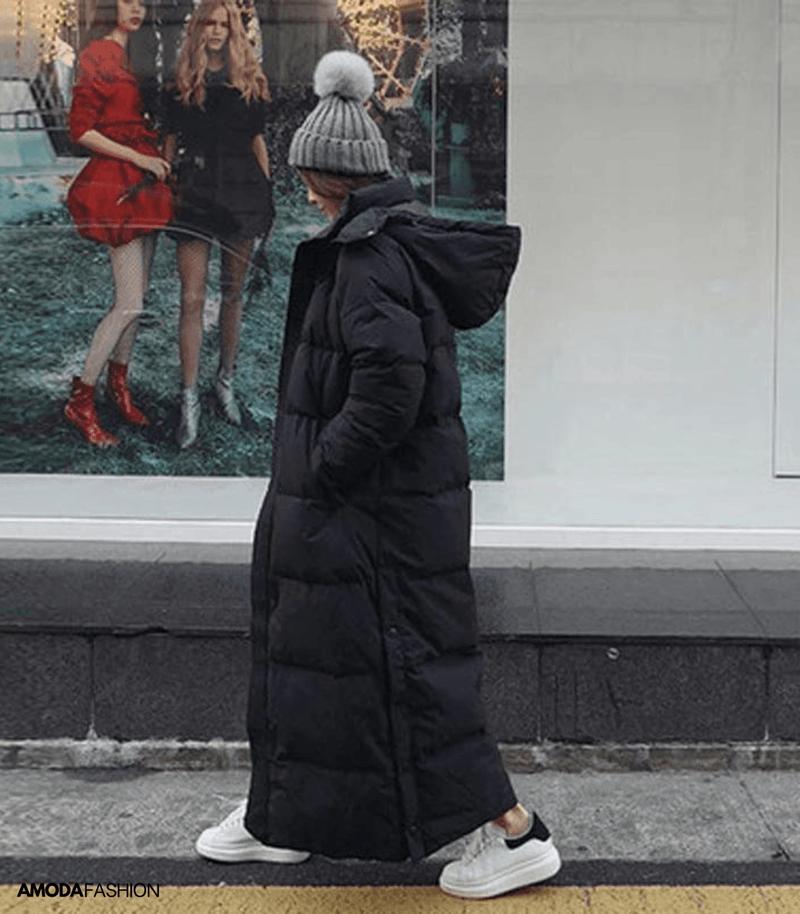 Frau im schwarzen, übergroßen Winterparka mit Kapuze, graue Mütze, weiße Sneaker, Stadtstraße.