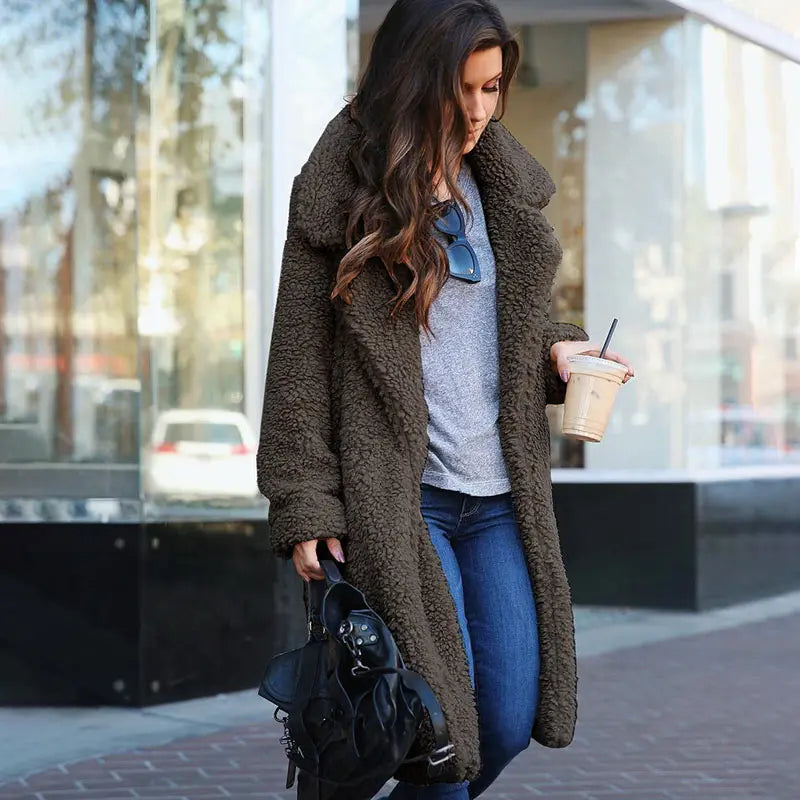 Frau in braunem Teddy-Mantel, Jeans, grauem Shirt, mit Kaffee und schwarzer Tasche auf der Straße.