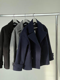 Drei Wollmäntel in Schwarz, Grau und Dunkelblau auf Kleiderstange, Herbstmode.