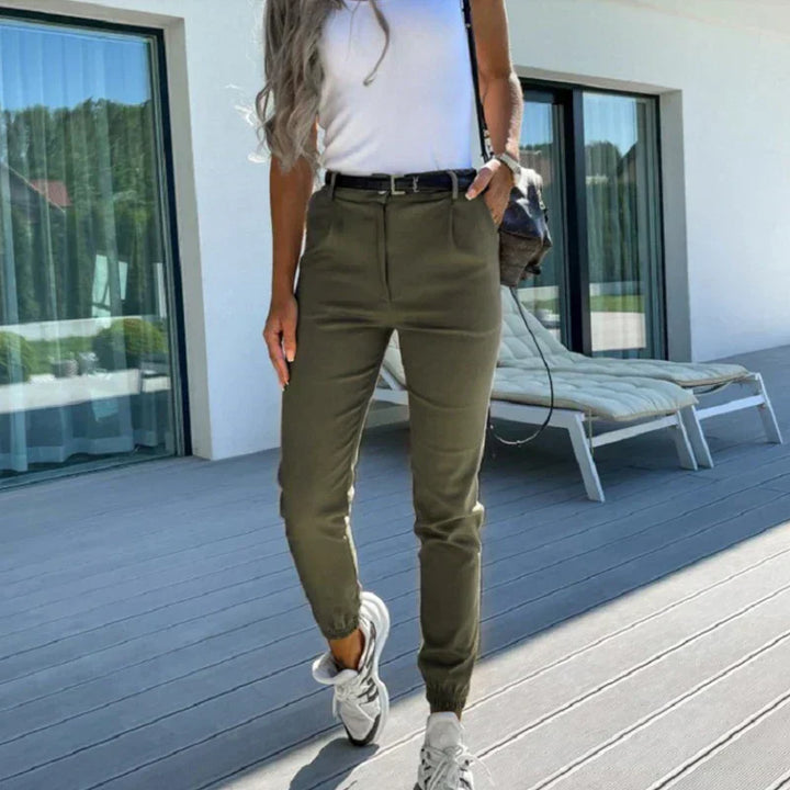 Frau in olivgrüner Hose und weißem Top auf Terrasse, lässiger Sommerlook, Mode 2023.