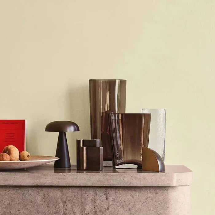 Moderne braune Glasvasen und schwarze Tischlampe auf Marmorkamin vor hellgrüner Wand.