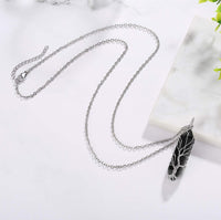 Silberne Halskette mit schwarzem Federanhänger auf Marmorhintergrund, Modeschmuck Accessoire.