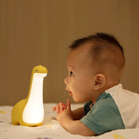 Gelbe Dinosaurier-Nachtlampe aus Silikon mit LED, neben Baby auf Bett, Kinderzimmer-Dekor.