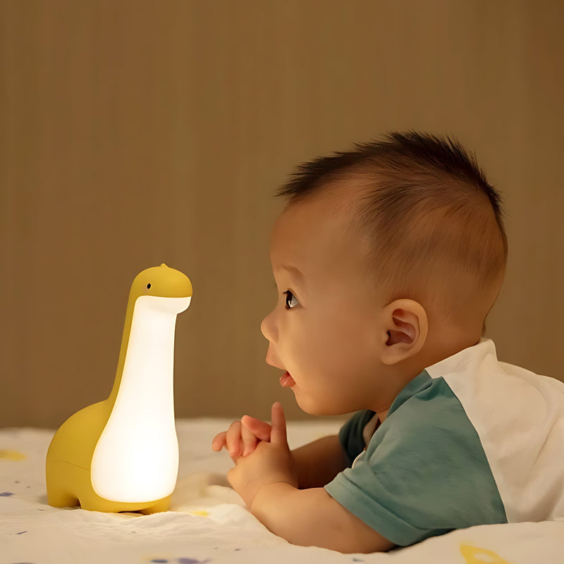 Gelbe Dinosaurier-Nachtlampe aus Silikon mit LED, neben Baby auf Bett, Kinderzimmer-Dekor.