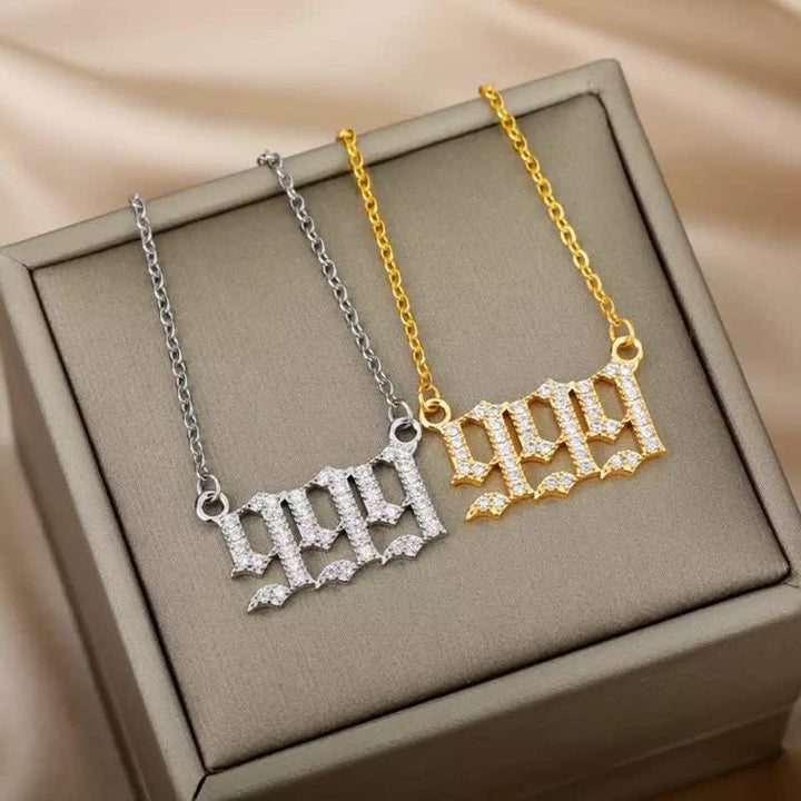 Zwei Halsketten mit "999"-Anhänger, eine in Silber, eine in Gold, auf beigem Hintergrund.