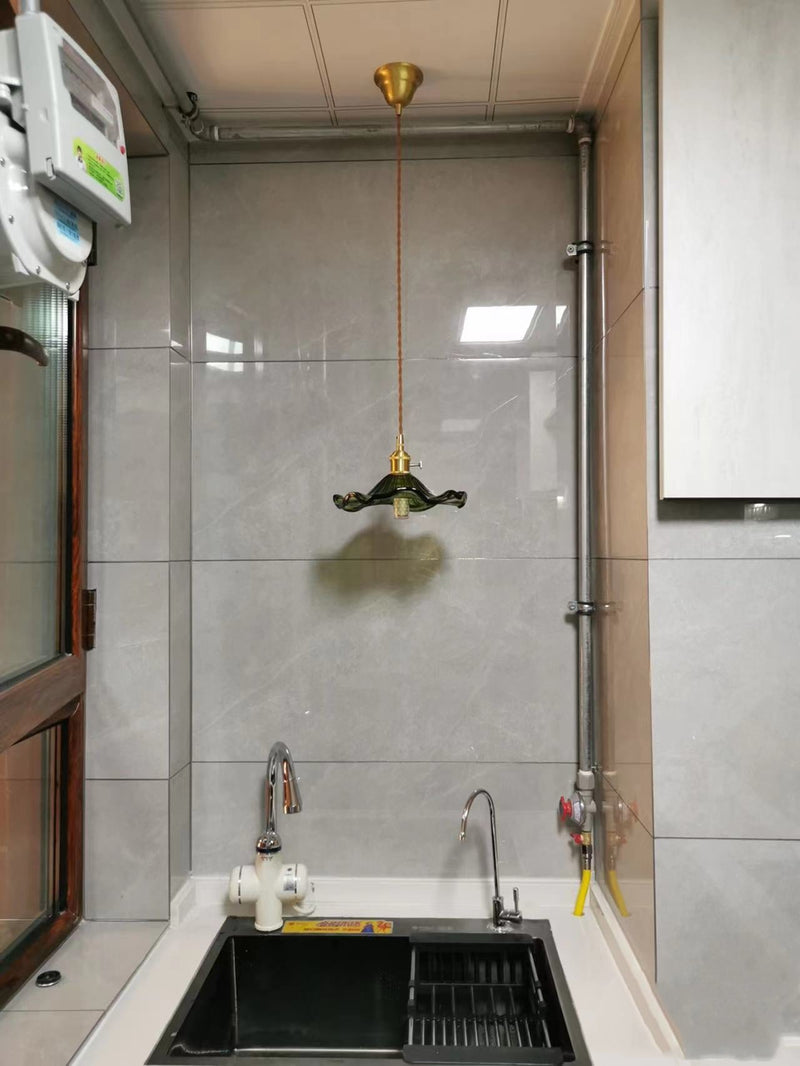 Küchenarmatur mit schwarzem Spülbecken, goldener Pendelleuchte, graue Fliesenwand.