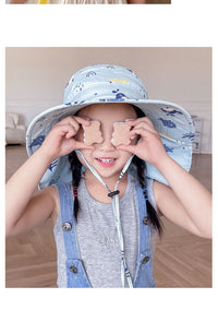 Mädchen mit blauem Sonnenhut und Keksen, lächelnd, graues Top, Zöpfe, Innenraum.