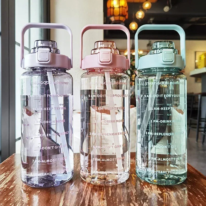 Drei transparente Wasserflaschen mit Zeitmarkierungen, rosa, lila und blau, auf Holztisch.