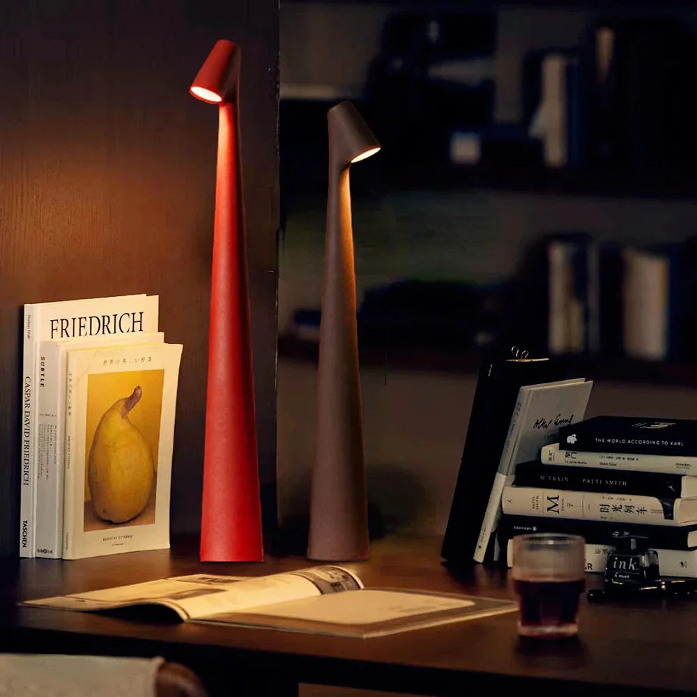 Zwei moderne LED-Tischlampen, rot und braun, auf einem Holzregal neben Büchern und einem Glas.