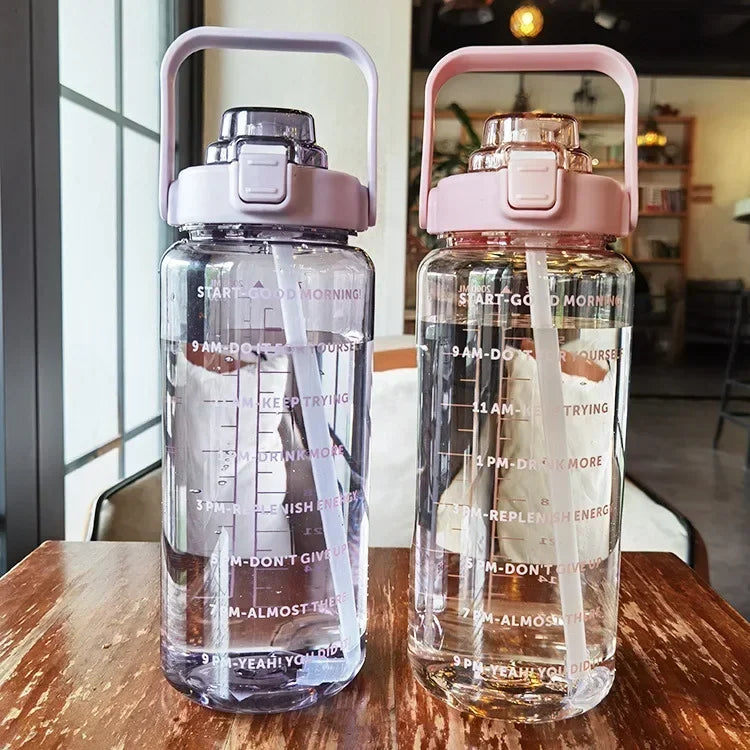 Zwei transparente Wasserflaschen mit rosa und lila Deckeln, Motivationsaufdruck, im Café.