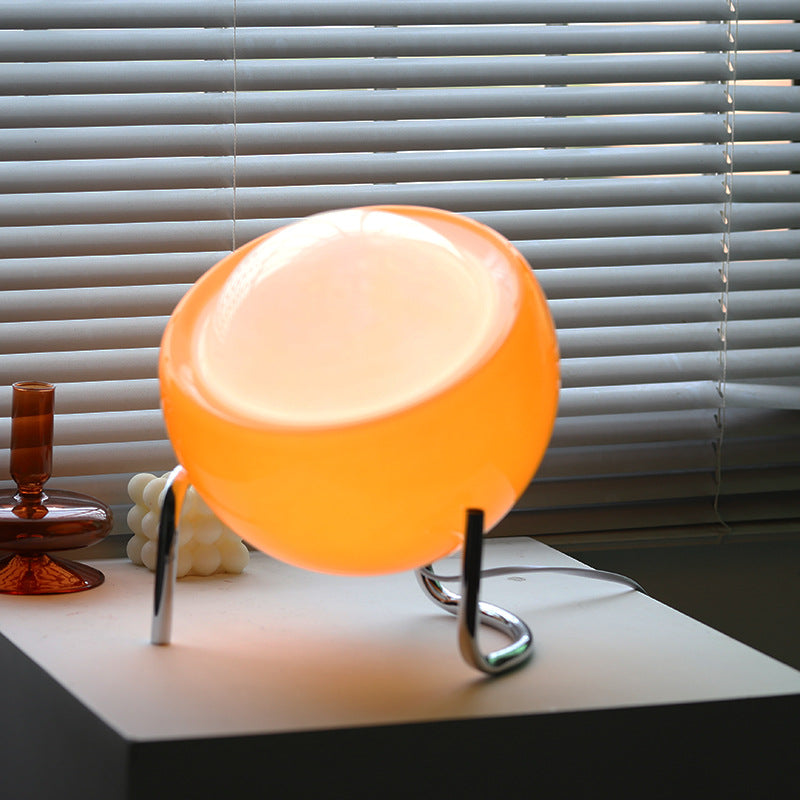 Orange Tischlampe aus Glas auf weißem Tisch vor Jalousien, modernes Design, Innenbeleuchtung.