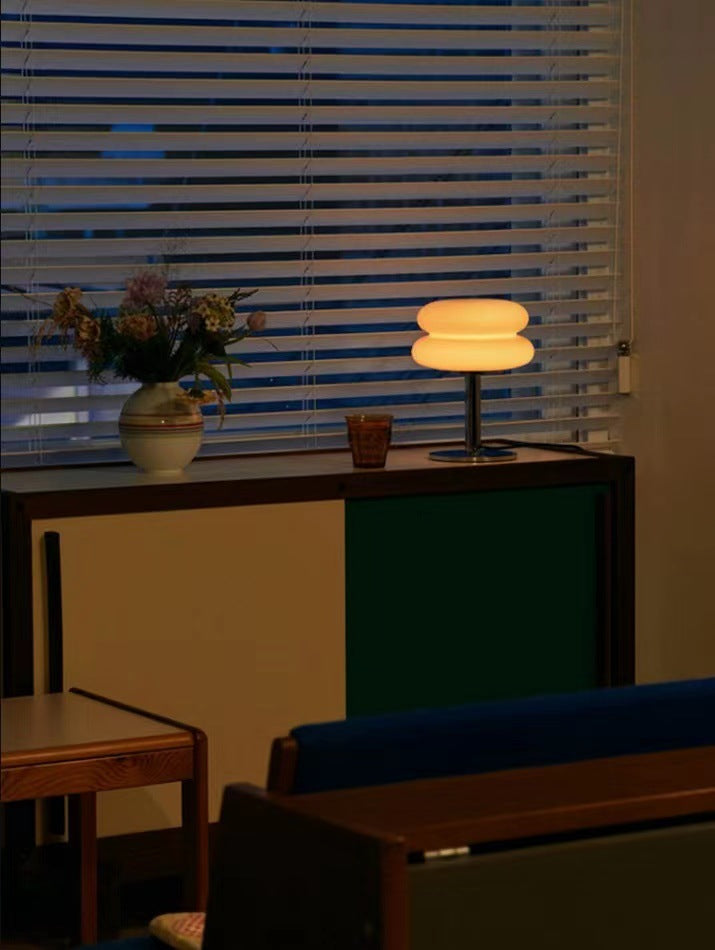 Moderne Tischlampe auf Sideboard, neben Blumenstrauß, vor Jalousien im Wohnzimmer.