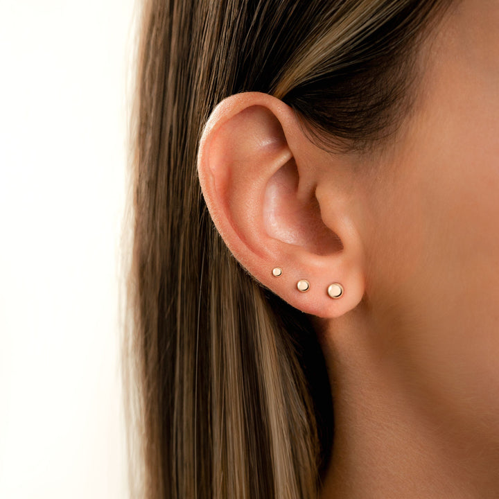 Frauenohr mit drei goldenen Ohrsteckern, minimalistischer Schmuck, Nahaufnahme.