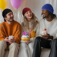 Drei lachende Freunde mit Mützen feiern Geburtstag mit Kuchen und Luftballons.