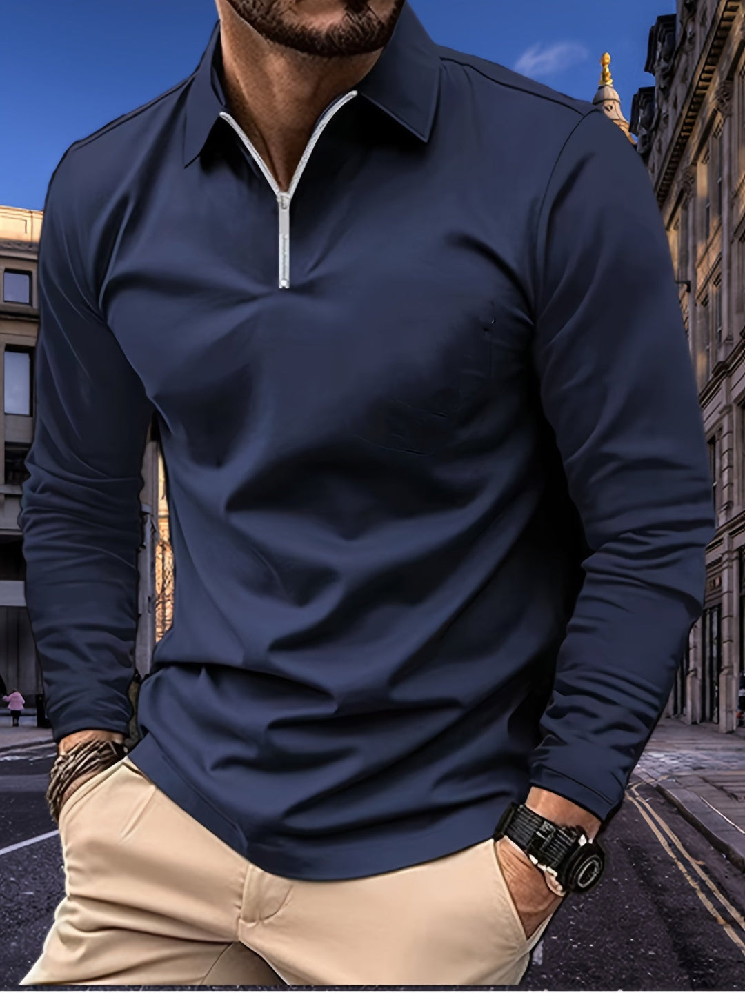 Mann in dunkelblauem Langarm-Poloshirt mit Reißverschluss, beige Hose, Stadt im Hintergrund.