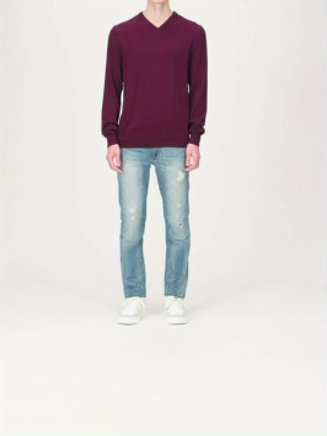 Person in burgunderrotem V-Ausschnitt-Pullover, hellblauer Jeans und weißen Sneakers.