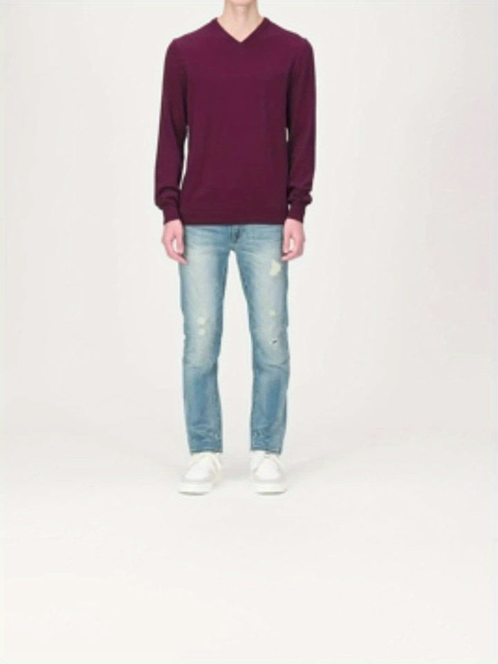 Person in burgunderrotem V-Ausschnitt-Pullover, hellblauer Jeans und weißen Sneakers.