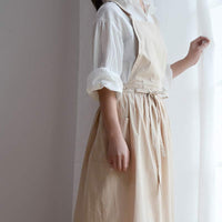 Frau in beiger Schürze und weißer Bluse am Fenster, Küchenschürze, Baumwolle, stilvoll.