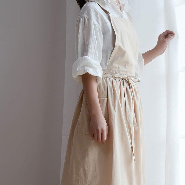 Frau in beiger Schürze und weißer Bluse am Fenster, Küchenschürze, Baumwolle, stilvoll.