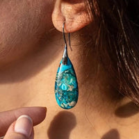 Türkisfarbener Tropfen-Ohrring aus Naturstein am Ohr einer Frau, eleganter Schmuck.