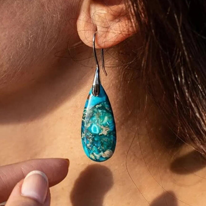 Türkisfarbener Tropfen-Ohrring aus Naturstein am Ohr einer Frau, eleganter Schmuck.