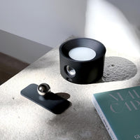 Schwarzer LED-Lautsprecher auf Tisch, modernes Design, neben Buch und Metallkugel.