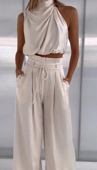 Damen-Outfit aus cremefarbenem Satin, ärmelloses Oberteil und weite Hose, elegant und modern.