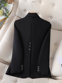 Schwarzer Blazer aus Wolle, Rückansicht, elegante Knöpfe, auf beigem Sessel drapiert.