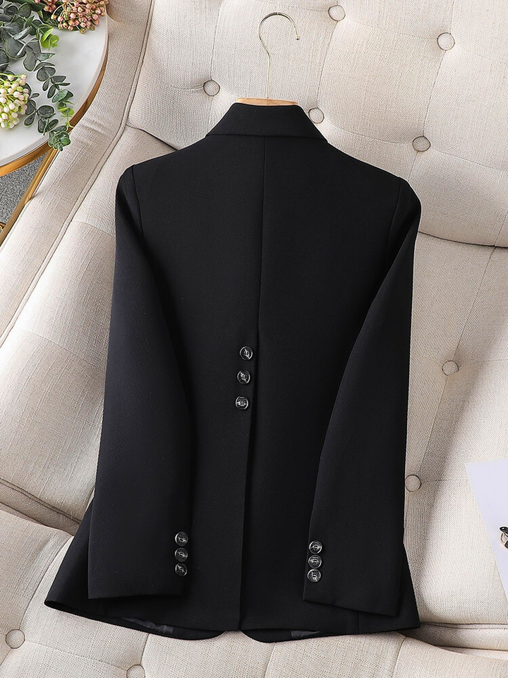 Schwarzer Blazer aus Wolle, Rückansicht, elegante Knöpfe, auf beigem Sessel drapiert.