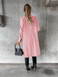 Frau in rosa Mantel, schwarze Stiefel, elegante Handtasche, Betonhintergrund.