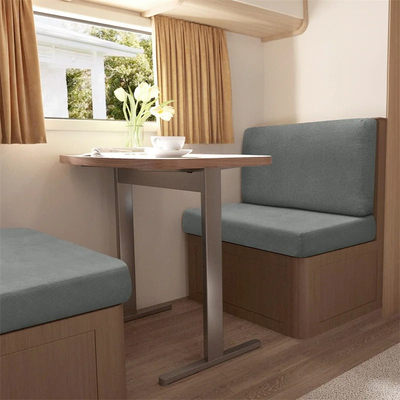 Wohnmobil-Essbereich mit grauen Polstern, Holztisch, Vorhängen und Blumen, gemütliches Interieur.