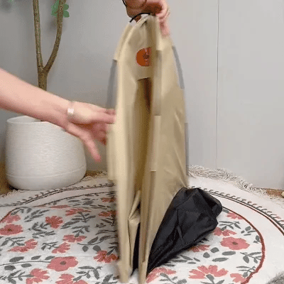 Person faltet tragbare, beige Hundebox aus Stoff auf gemustertem Teppich.