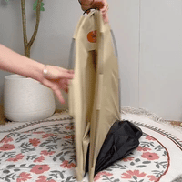 Person faltet tragbare, beige Hundebox aus Stoff auf gemustertem Teppich.