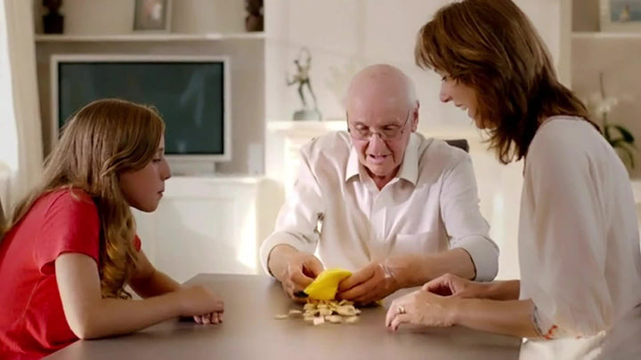 Esstisch mit drei Personen, die Bananen schälen, helle Küche, familiäre Atmosphäre.