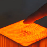 Finger berührt leuchtende Holzlampe, warmes Licht, modernes Design, stimmungsvolle Beleuchtung.