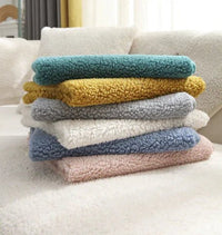 Stapel bunter, flauschiger Sofabezüge aus Plüschstoff auf weißem Sofa.