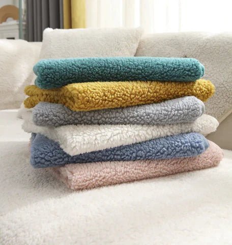 Stapel bunter, flauschiger Sofabezüge aus Plüschstoff auf weißem Sofa.