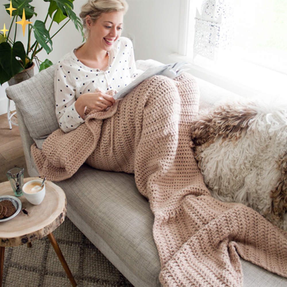 Frau liest auf Sofa mit rosa Strickdecke, Kaffeetasse, gemütliches Wohnzimmer, entspannte Atmosphäre.