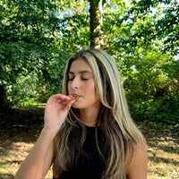 Frau im Wald mit schwarzem Top, isst Schokolade, Natur, Entspannung, Genussmoment.