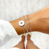Drei silberne Armbänder mit Sternanhänger und Strasssteinen auf Handgelenk.