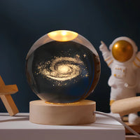 Leuchtende Galaxie-Kristallkugel auf Holzsockel, dekorative Lampe, Astronautenfigur im Hintergrund.