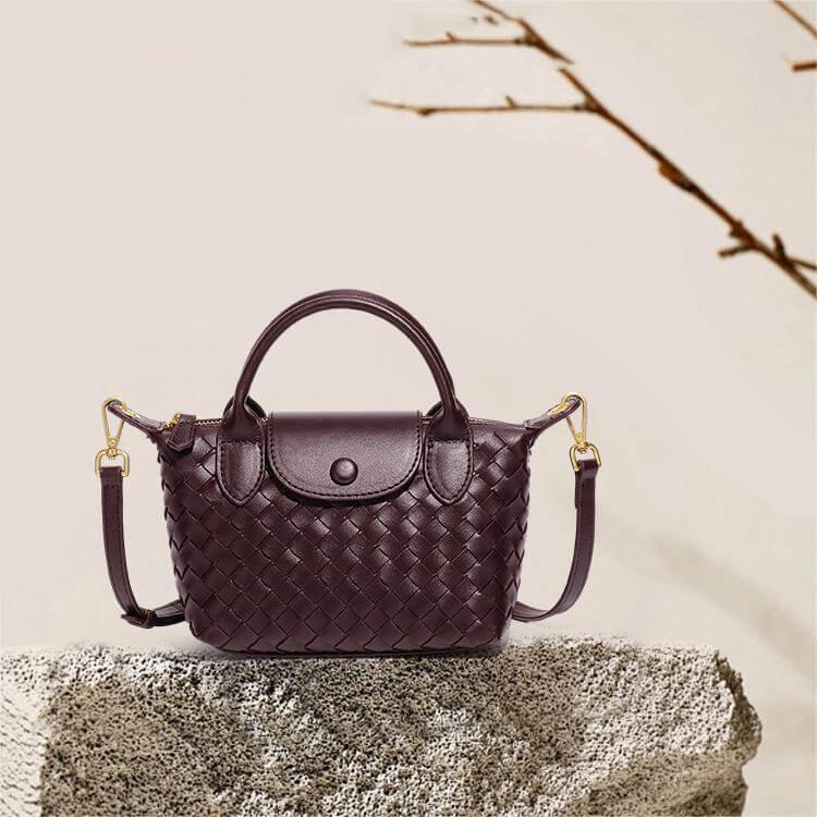 Geflochtene Handtasche aus Leder in Dunkelbraun mit Schulterriemen auf Steinuntergrund.